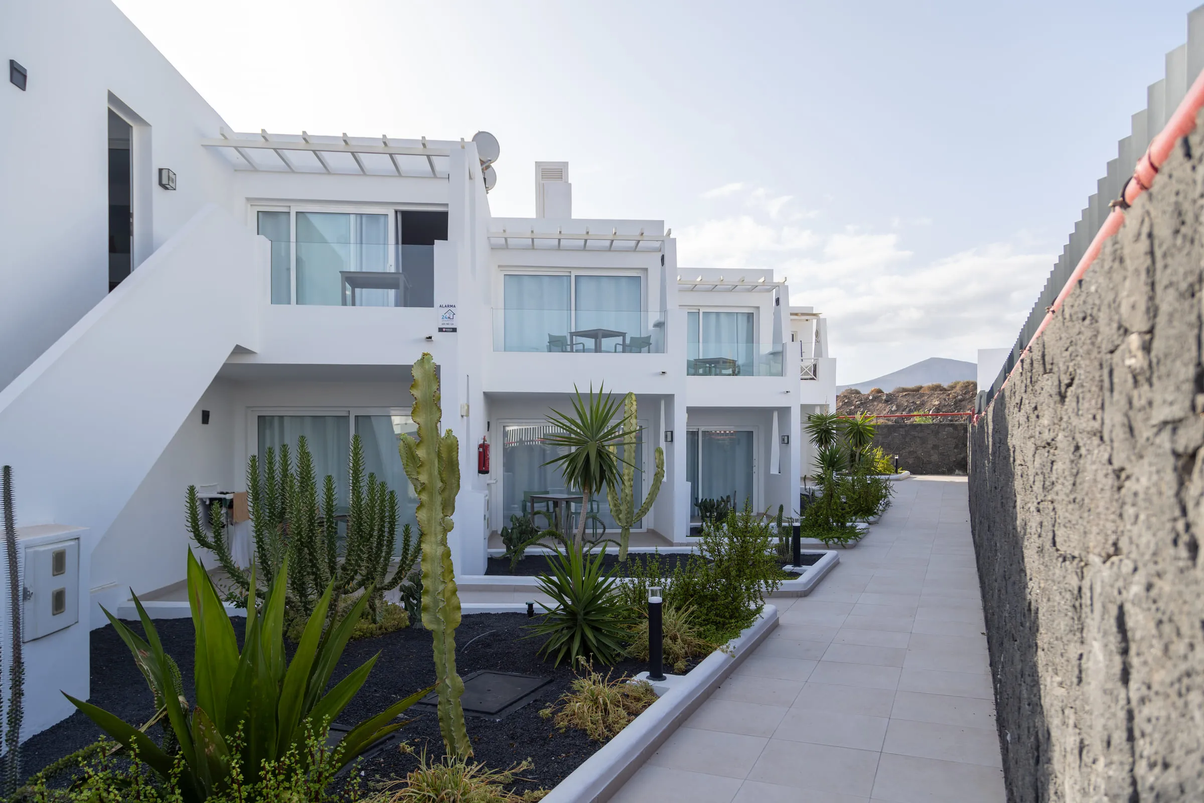The white apartment blocks at Tinasoria, with balconies and pergolas above a planted walkway of cacti and palms.