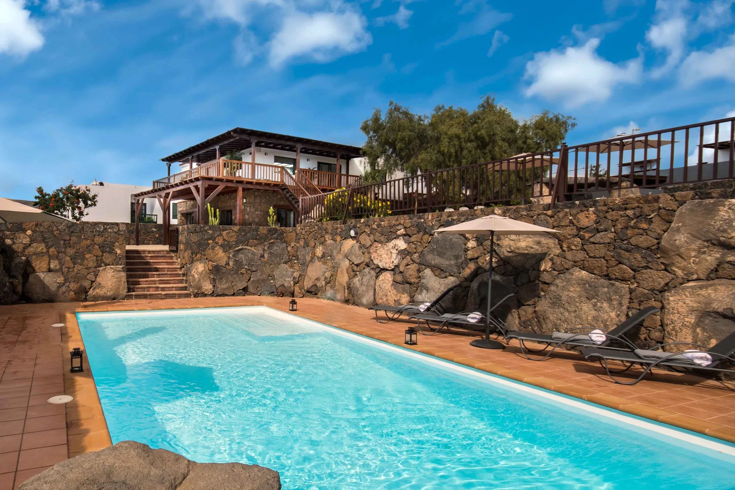 The villa seen from its private pool, a white house with a wooden balcony above a lava-stone wall.